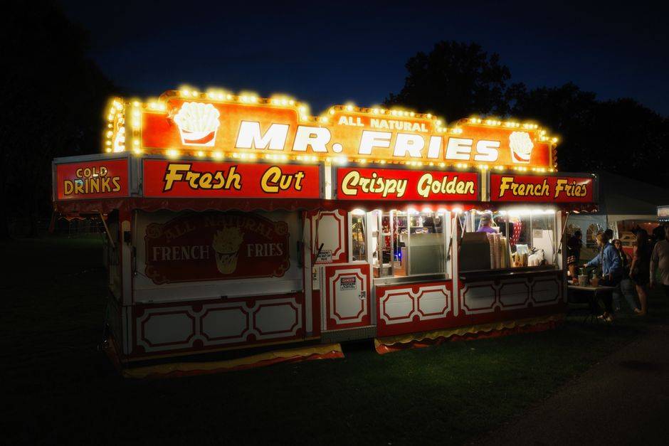 Brightly lit French fry stand at a nighttime festival offering fresh cut crispy fries.