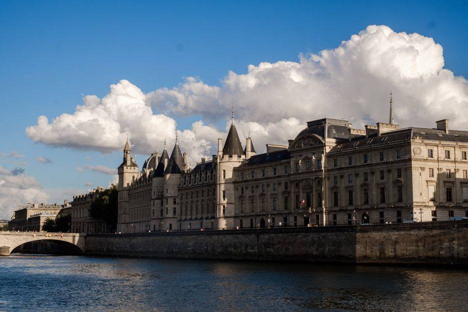 Capture of the historic Conciergerie palace by the Seine River in Paris under a bright blue sky.
